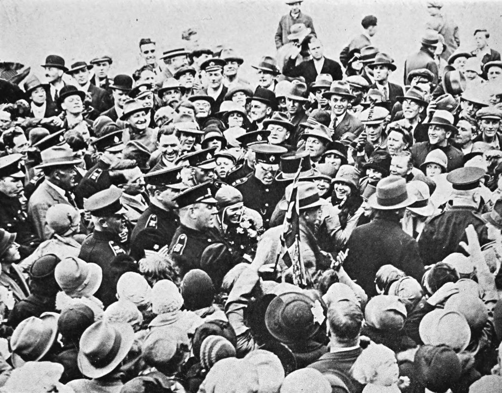 Photo wide overhead shot of Earhart in flight
                gear escorted by police through a crowd